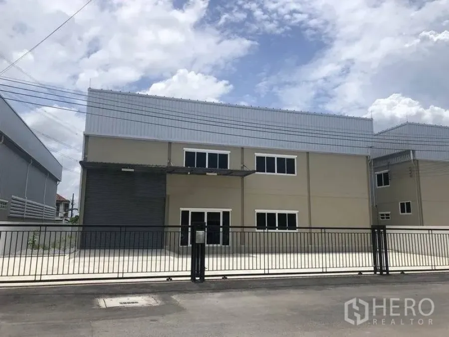Warehouse for rent or sale in Bang Phli, Samut Prakan - Modern two-storey warehouse with metal roof, roller shutter loading bay, office windows, and gated concrete yard in Bang Phli.