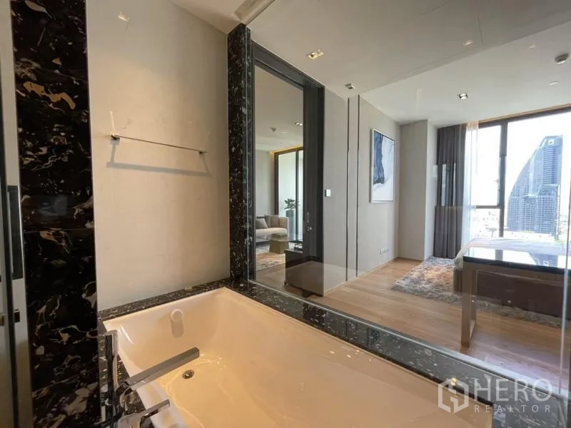 Condominium for rent in Khlong Toei, Bangkok - Contemporary bathroom with soaking tub, marble accents, and glass wall looking into the bedroom and living area.