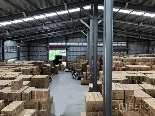 Warehouse for rent in Nonthaburi - Spacious warehouse interior with steel structure and stacks of cardboard boxes on the floor.