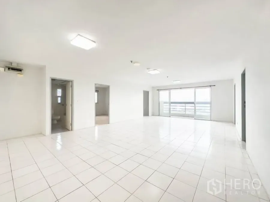 Condominium for sale in Bang Na, Bangkok - Spacious white-tiled living room with sliding glass doors opening to a balcony and city view.
