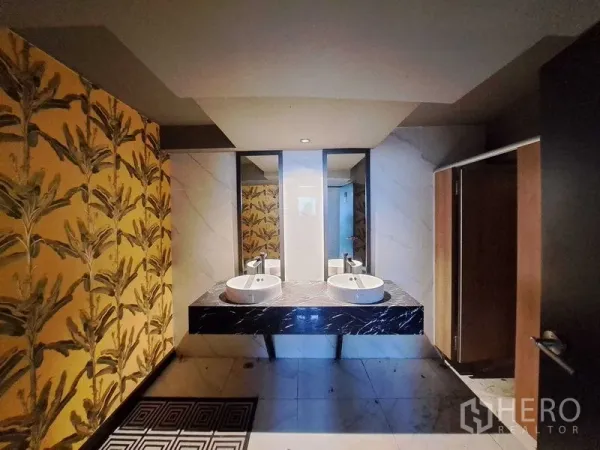 Retail Space for rent in Watthana, Bangkok - Restroom with dual vessel sinks on a black marble vanity, mirrors, and tropical patterned walls.