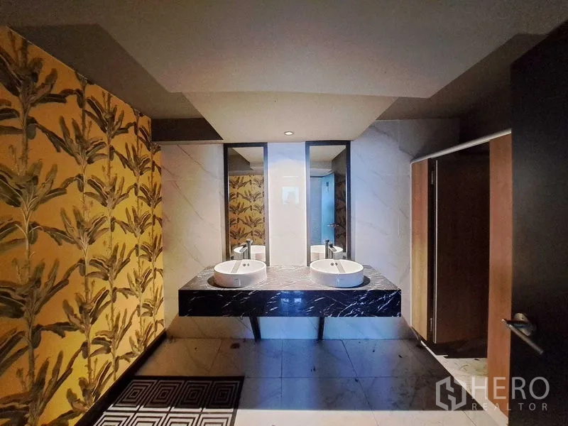 Retail Space for rent in Watthana, Bangkok - Restroom with dual vessel sinks on a black marble vanity, mirrors, and tropical patterned walls.