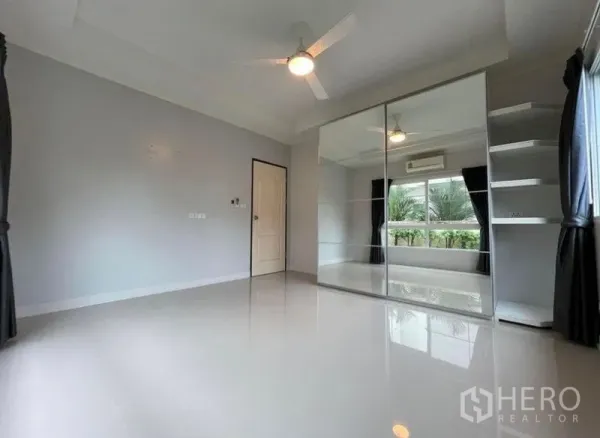 Detached House for sale in Bang Phli, Samut Prakan - Spacious bedroom with mirrored wardrobe, ceiling fan and a large window facing greenery.