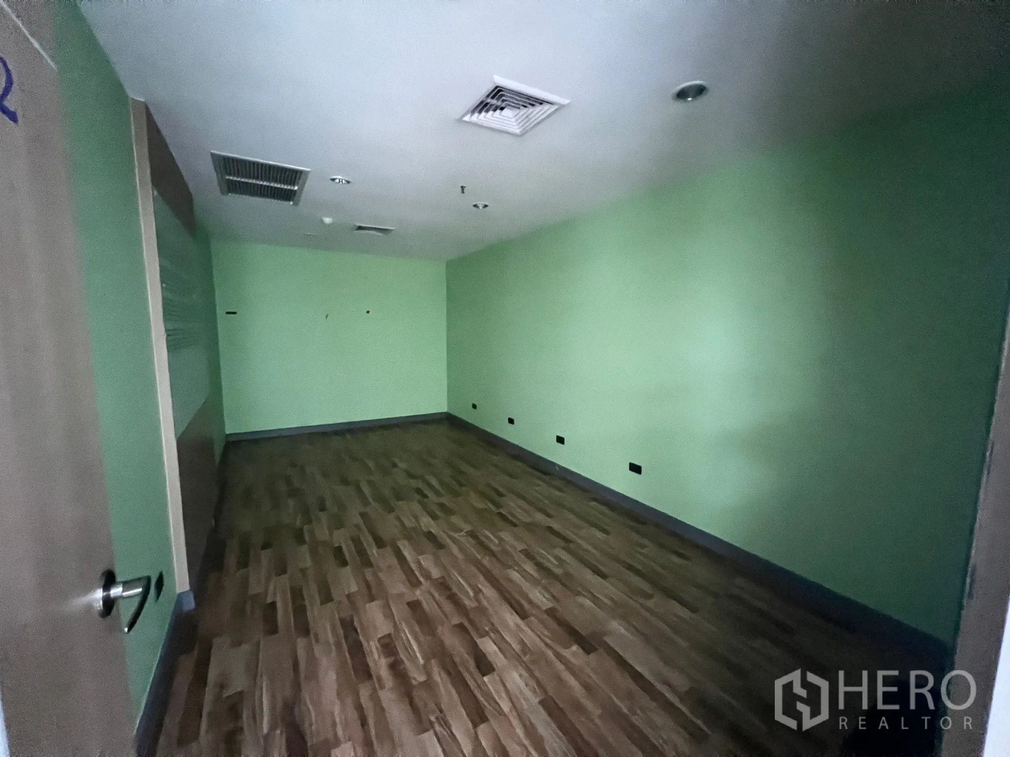 Retail Space for rent - Large partitioned room with green walls, wood-effect floor and ceiling air-conditioning vents.
