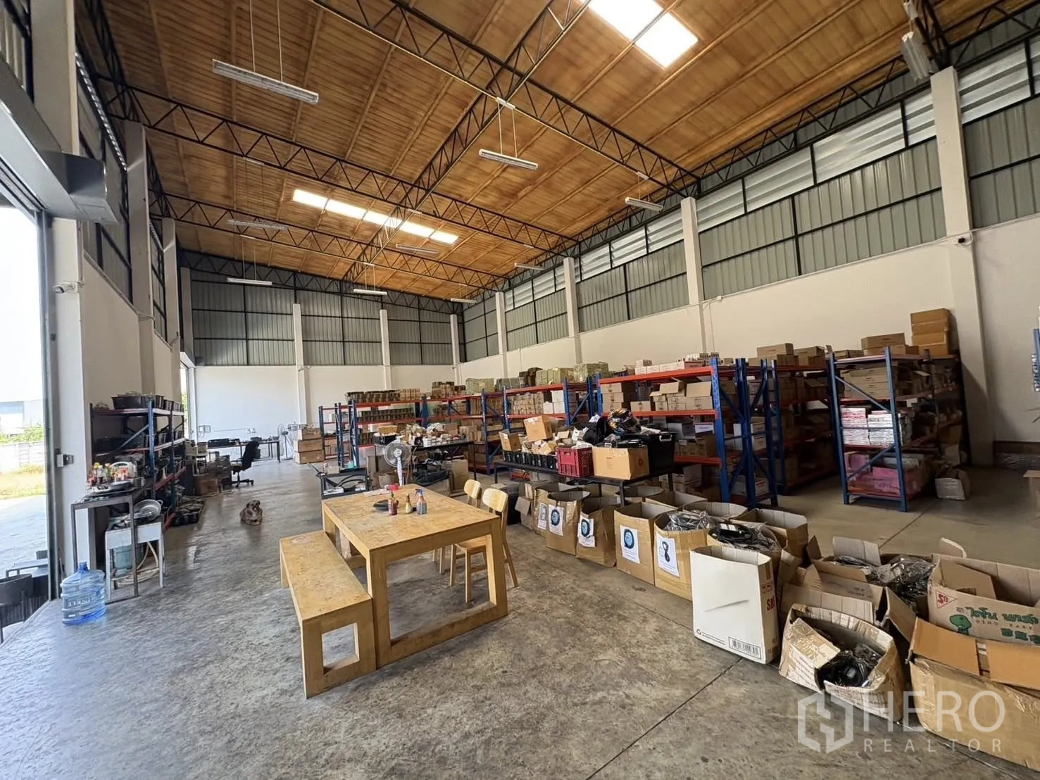 Factory for rent or sale in Bang Len, Nakhon Pathom - High-ceiling warehouse interior with steel trusses, skylights, concrete floor, and storage racks.