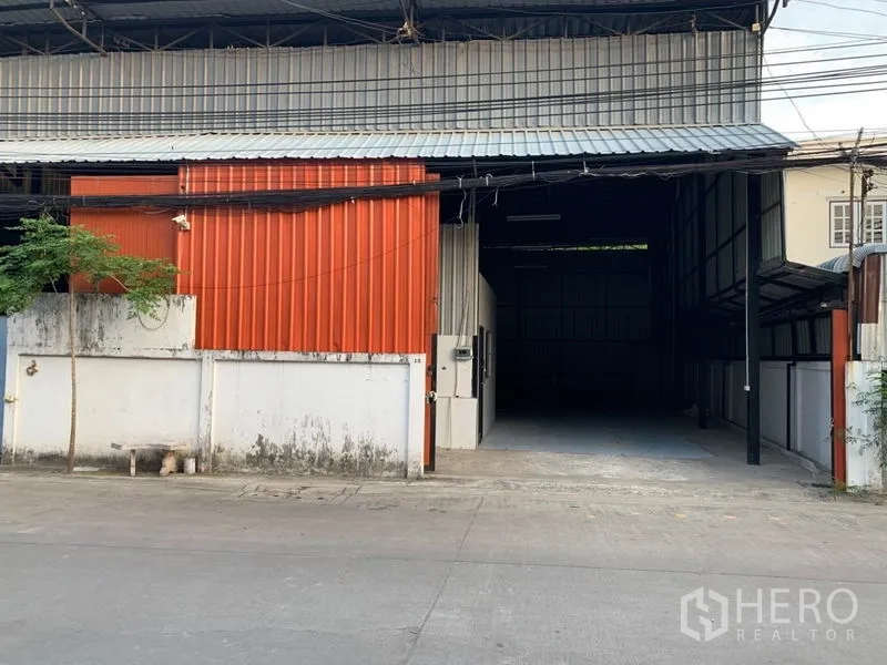 Warehouse for rent in Bang Kapi, Bangkok - Street view of a steel-clad warehouse with orange facade and a wide vehicle entrance in Bang Kapi.