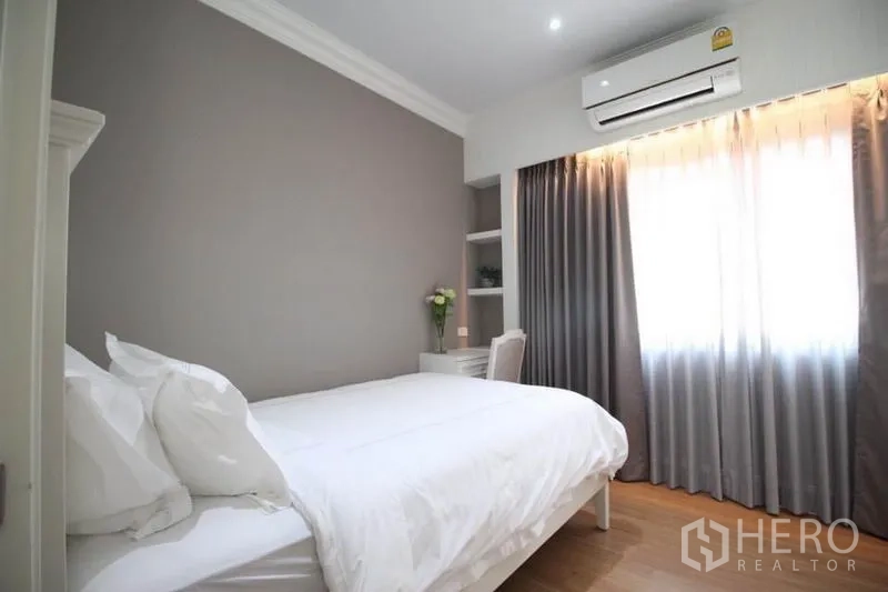 Detached House for rent or sale in Lat Phrao, Bangkok - Secondary bedroom with double bed, gray accent wall and small desk by the window.