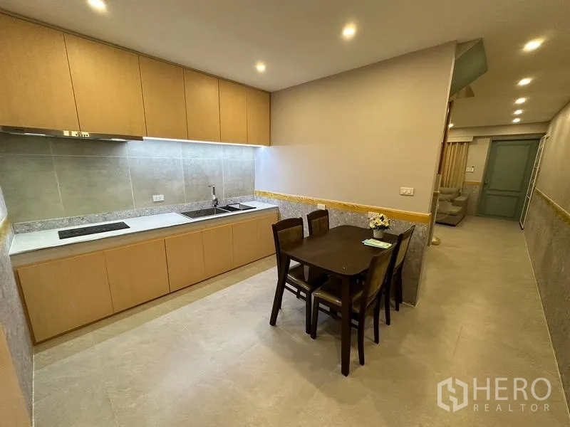 联排别墅 出租在Phra Khanong, Bangkok - 整体厨房配浅木柜、电炉、水槽与四人餐桌。