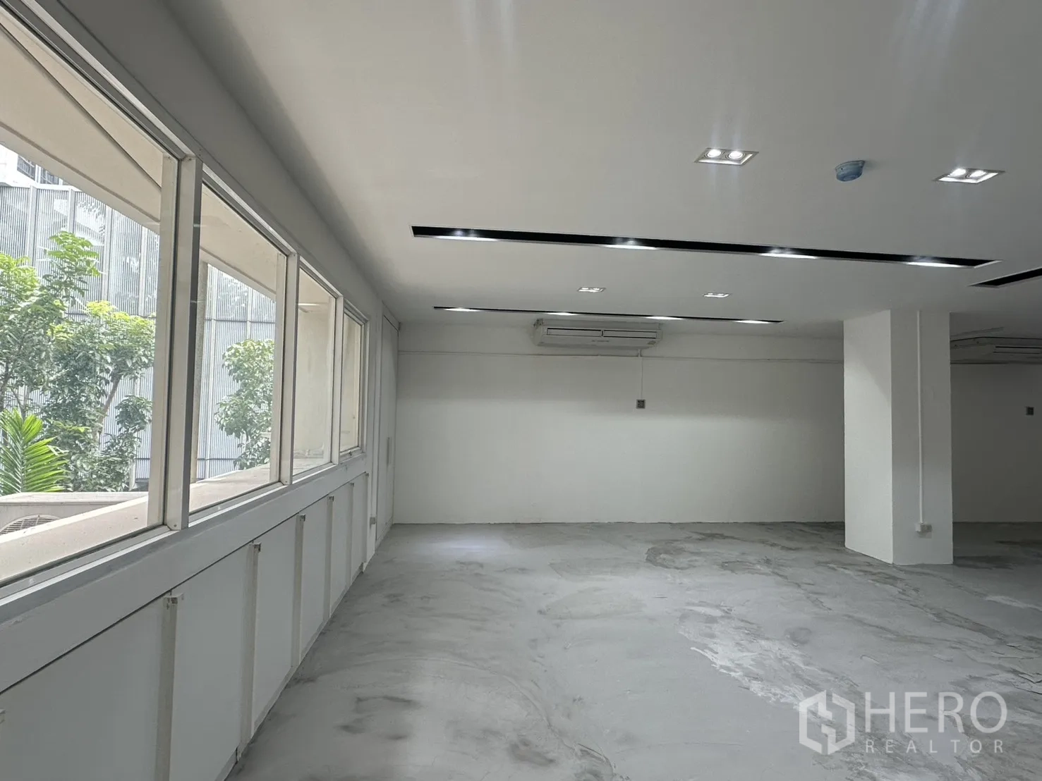 Office Space for rent in Pathum Wan, Bangkok - Row of large windows with greenery outside and split-type air conditioners.