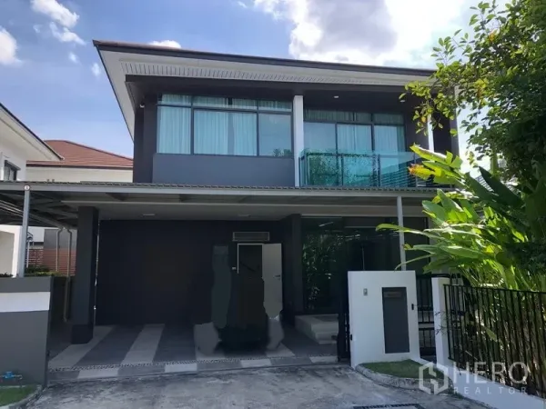 Detached House for rent in Bang Kapi, Bangkok - Front view of a modern two-storey detached house with carport, balcony and gate amid greenery in Bang Kapi.