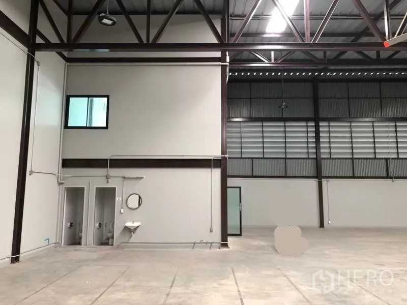 Warehouse for rent in Bang Phli, Samut Prakan - Warehouse interior corner with high steel beams, two restrooms and a wall-mounted sink.
