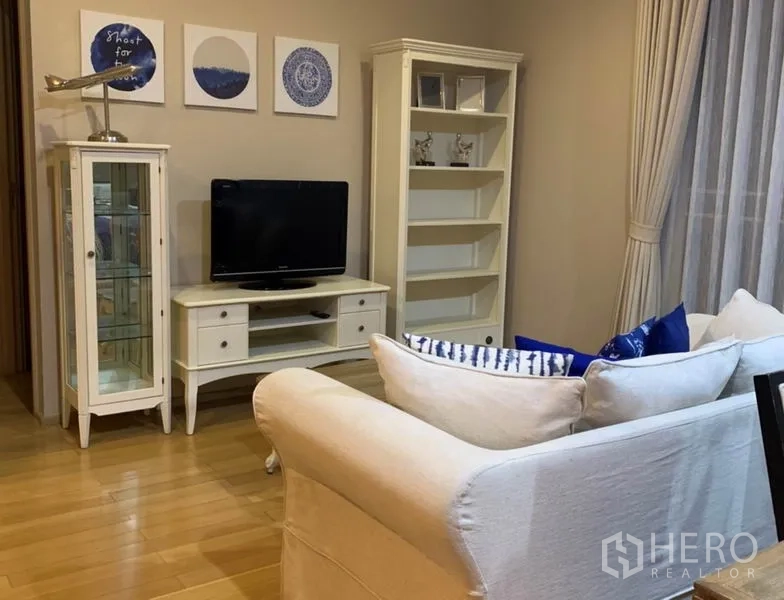 Condominium for rent in Watthana, Bangkok - Cozy lounge with white TV console, glass display cabinet, open shelving and floor-to-ceiling curtains.