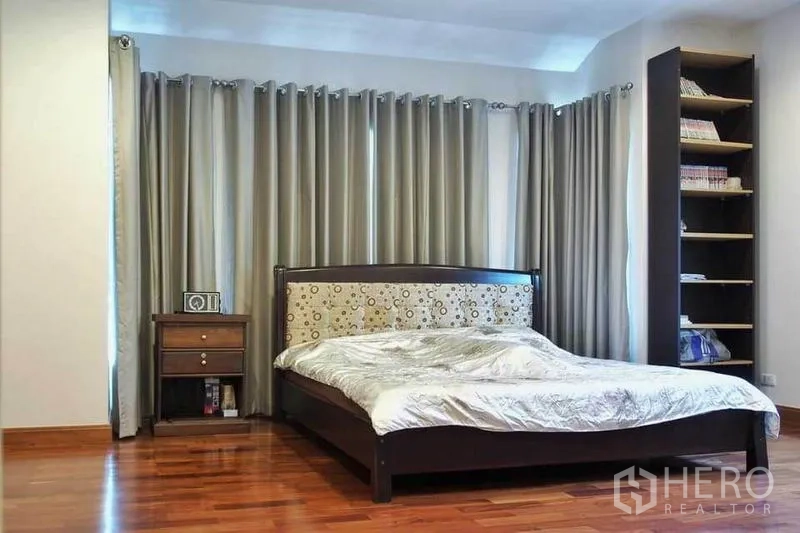 Detached House for rent or sale in Pak Kret, Nonthaburi - Bright secondary bedroom with tall bookshelf, full-length curtains and polished wooden floor.