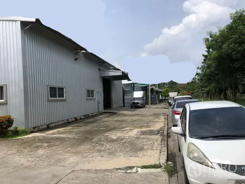 Warehouse for rent in Pak Kret, Nonthaburi - Driveway alongside warehouse buildings with car and truck parking and wide access for loading.