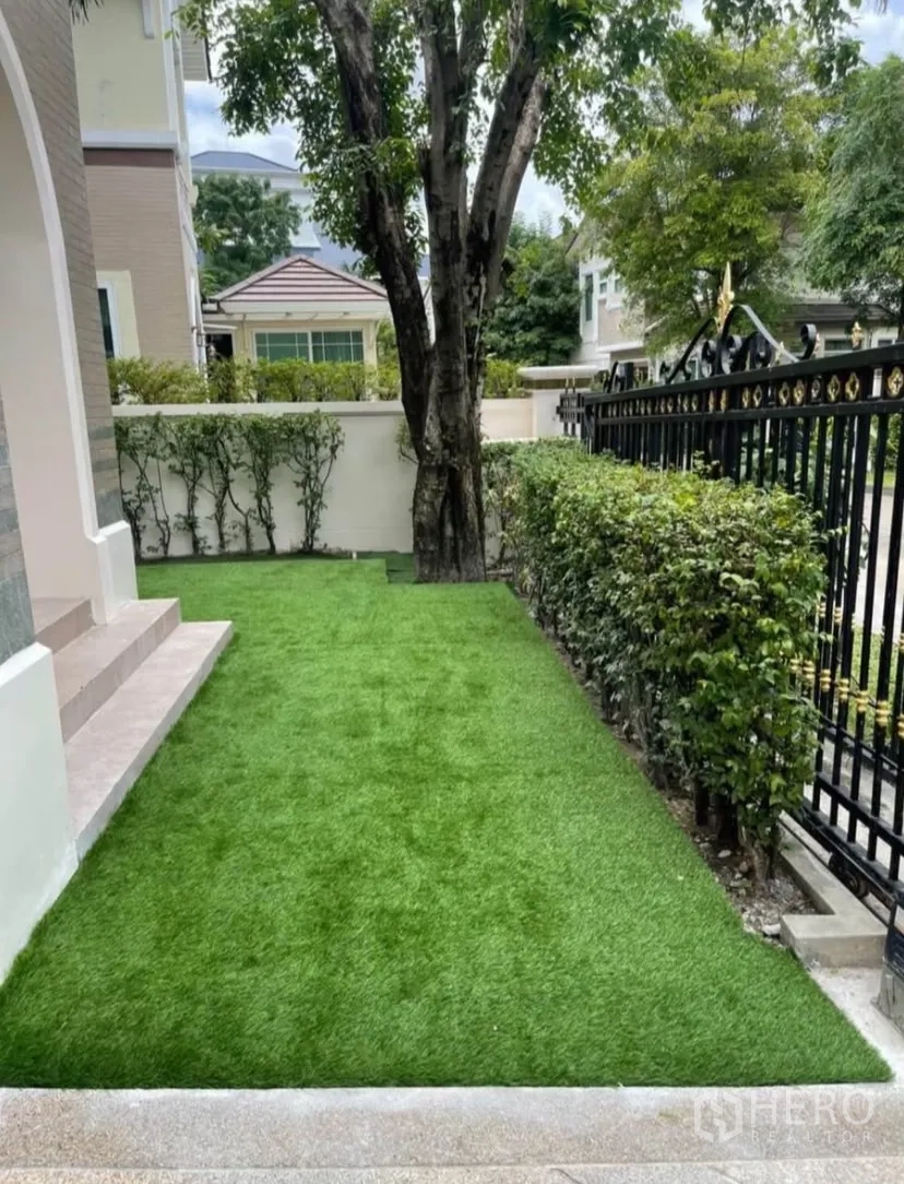 独立式住宅 出租或出售在Lat Phrao, Bangkok - 前庭草坪整洁，树木与铁艺围栏。