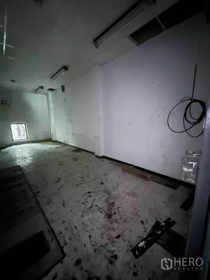 零售空间 出租在Watthana, Bangkok - 光线较暗的零售空间，白墙、后侧小窗与外露线路，待翻新。
