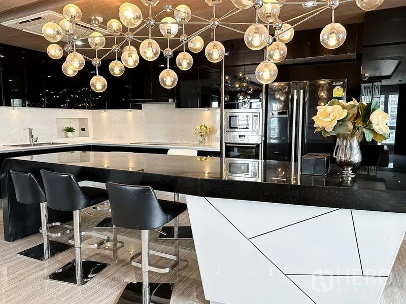 Condominium for rent or sale in Khlong Toei, Bangkok - Kitchen island with bar stools beneath a sculptural globe chandelier.