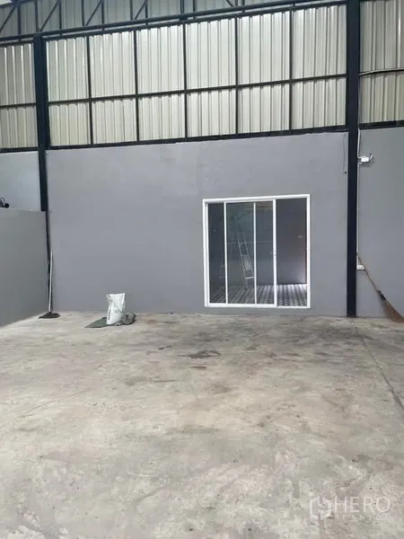 Warehouse for rent in Saphan Sung, Bangkok - Close-up of the warehouse office with white sliding glass doors set into a gray wall.