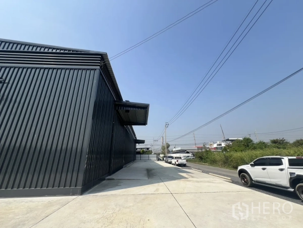Warehouse for rent in Lat Krabang, Bangkok - Access road and parking alongside the warehouse with a broad yard and utility lines.