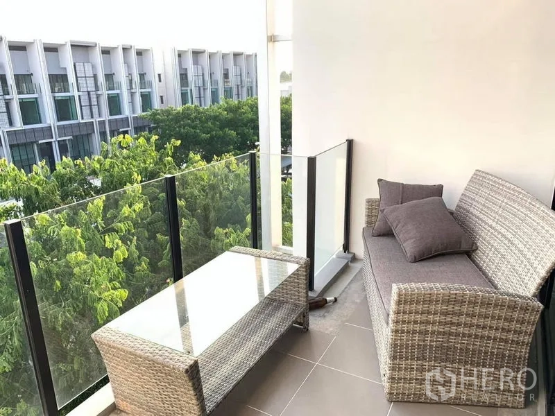 Home Office for rent - Balcony with rattan sofa and glass table overlooking green trees and neighboring buildings.