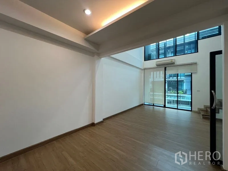 Townhouse for rent or sale in Khlong Toei, Bangkok - Double-height living area with floor-to-ceiling windows and balcony access.