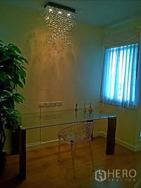 Condominium for rent in Pathum Wan, Bangkok - Quiet study corner with a glass desk, clear chair, window blinds, and a modern chandelier.