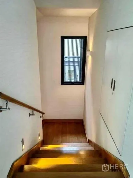 Detached House for sale in Huai Khwang, Bangkok - Wooden staircase with handrail, wall lights and a small window along the landing.