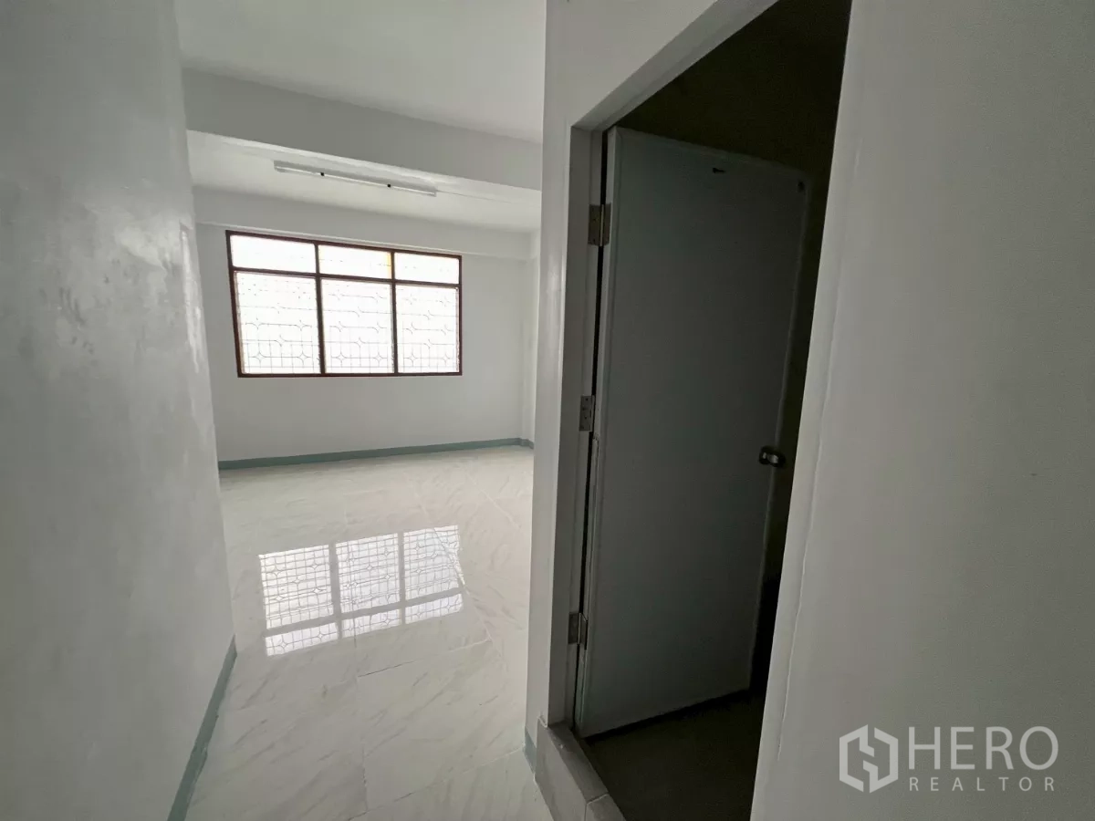 店屋 出租在Khlong Toei, Bangkok - 过道通向明亮铺砖房间与窗户，前景可见门框。