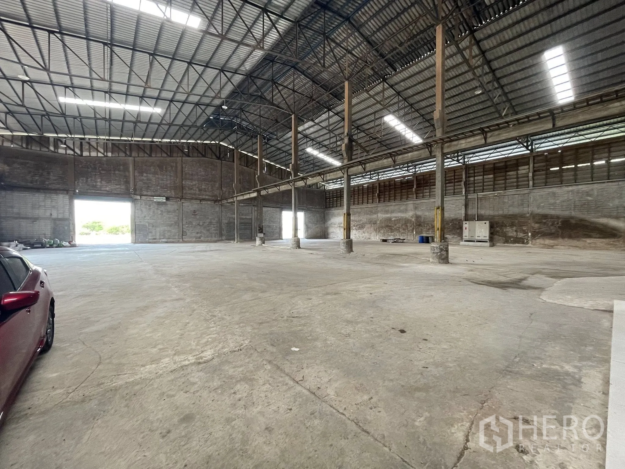 Factory for rent in Bang Bua Thong, Nonthaburi - Interior view showing multiple large roller doors, concrete floor, and skylight panels.