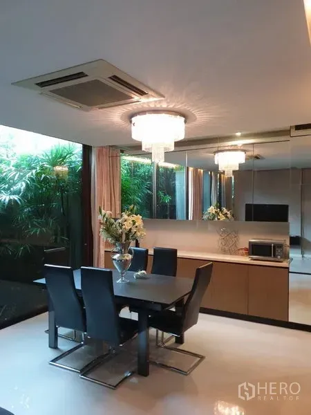 Detached House for sale in Watthana, Bangkok - Dining area with crystal chandelier, mirror wall and garden view.