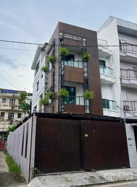 联排别墅 出租在Phaya Thai, Bangkok - 现代多层联排别墅外立面，木质装饰、玻璃阳台与垂直绿植，高门庭院。