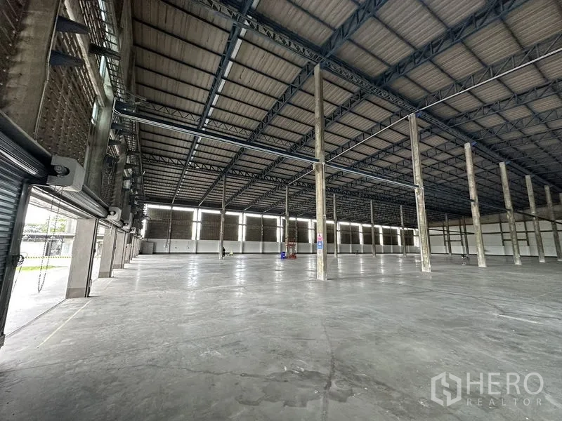 Factory for rent in Bang Sao Thong, Samut Prakan - Wide interior showing several roller shutter doors along the side wall and ample natural light.