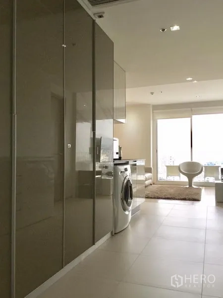 Condominium for rent or sale in Watthana, Bangkok - Hallway view of sleek kitchen cabinetry leading to a sunlit living room.