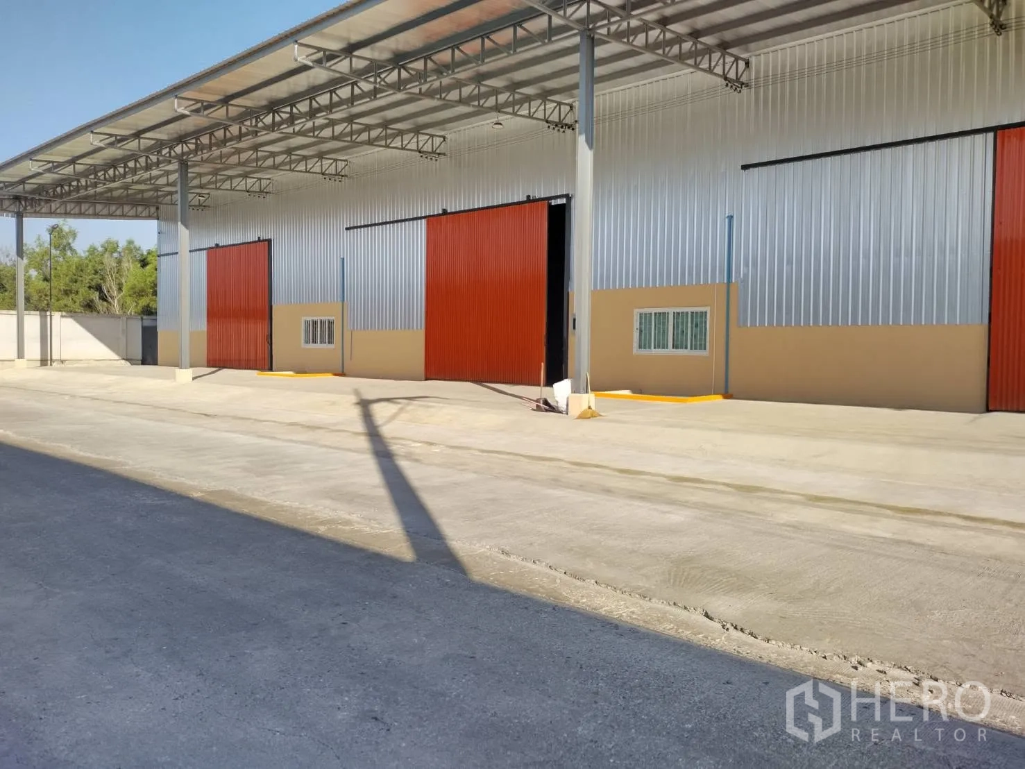 Warehouse for rent in Khlong Luang, Pathum Thani - Warehouse facade with an open sliding door, steel columns, and a deep concrete apron for loading and parking.