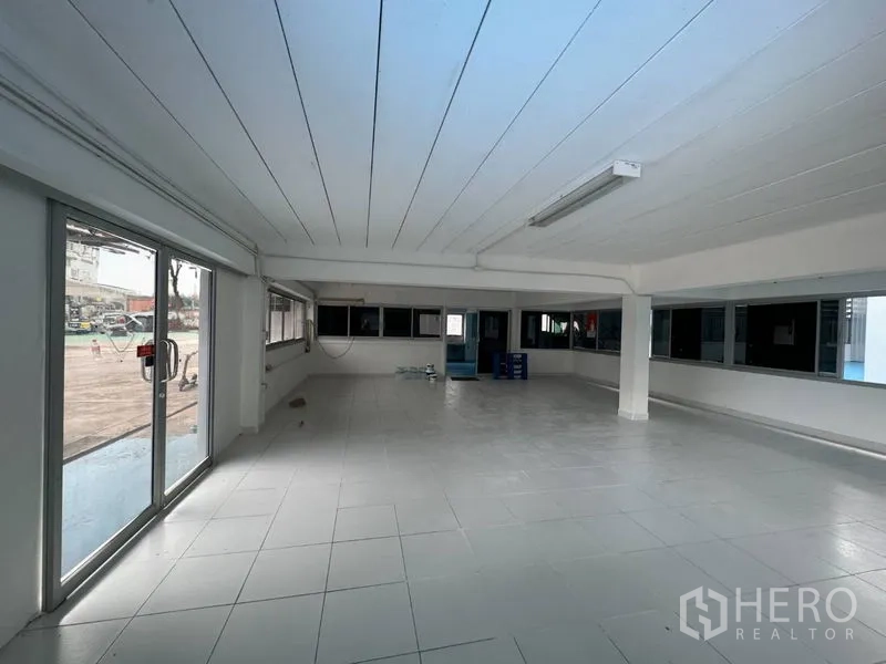 Warehouse for rent in Mueang Pathum Thani, Pathum Thani - Ground-floor office room with tile floor and glass doors opening toward the paved yard.