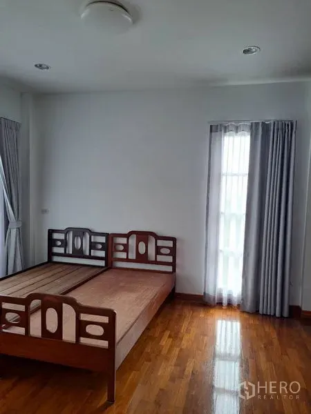 Detached House for rent in Prawet, Bangkok - Bedroom with wooden bed frame, hardwood floor and tall curtained windows.