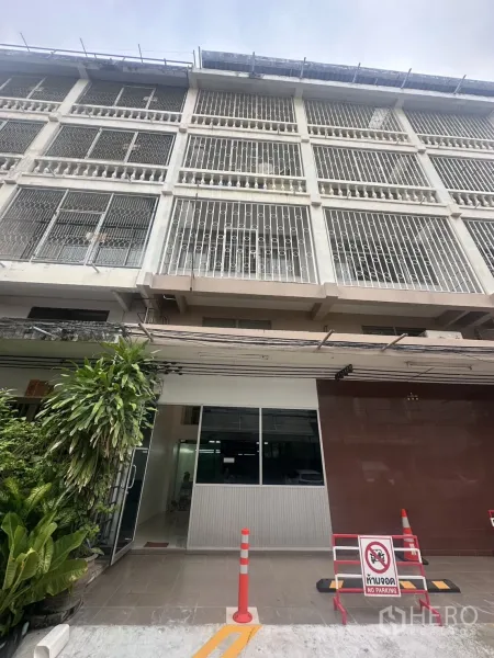 Office Space for rent in Khlong Toei, Bangkok - Multi-storey office building facade with metal grilles, glass entry, plants and no-parking signs.