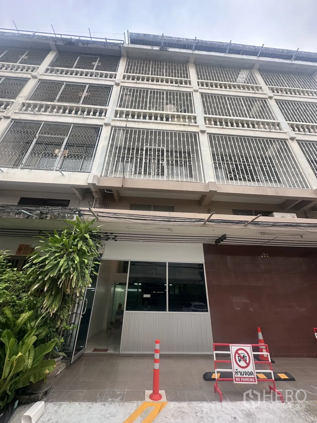 Office Space for rent in Khlong Toei, Bangkok - Multi-storey office building facade with metal grilles, glass entry, plants and no-parking signs.