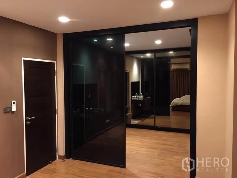 Detached House for rent or sale in Khlong Toei, Bangkok - Bedroom dressing area with black glass sliding doors and mirrored wardrobe on wood floors.