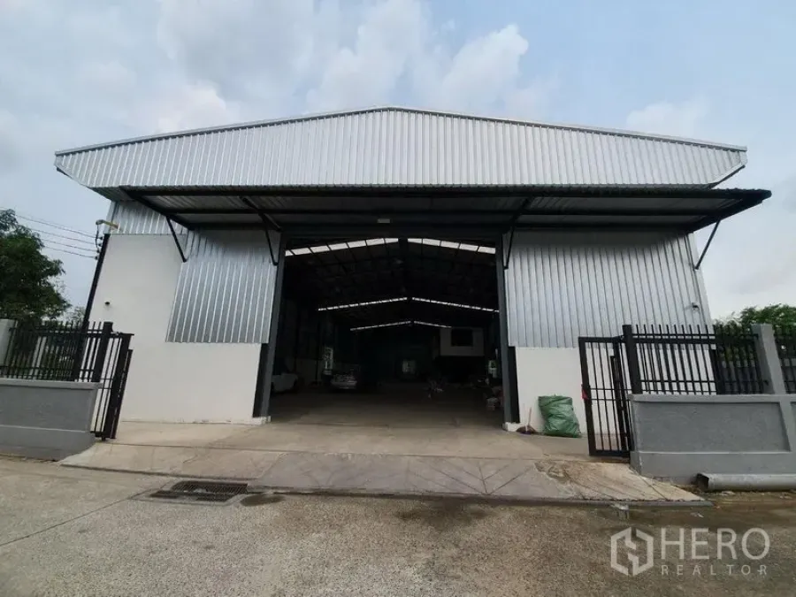 Warehouse for rent in Bang Khen, Bangkok - Gated steel-clad warehouse facade with wide open entrance and pitched roof on a concrete forecourt.