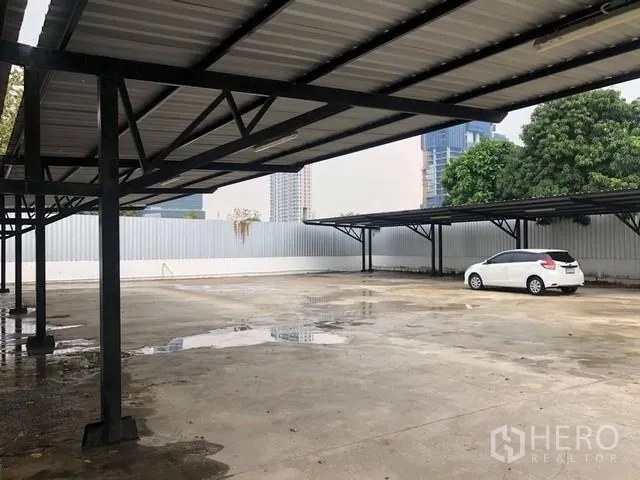 地 出租在Phra Khanong, Bangkok - 硬化混凝土场地，钢结构遮棚与围墙，远景城市天际线。
