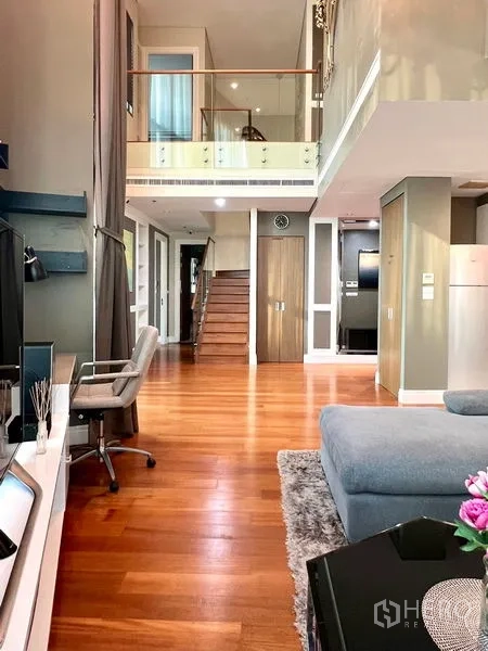 Condominium for rent in Khlong Toei, Bangkok - Living room toward staircase with TV console and lofted ceiling.