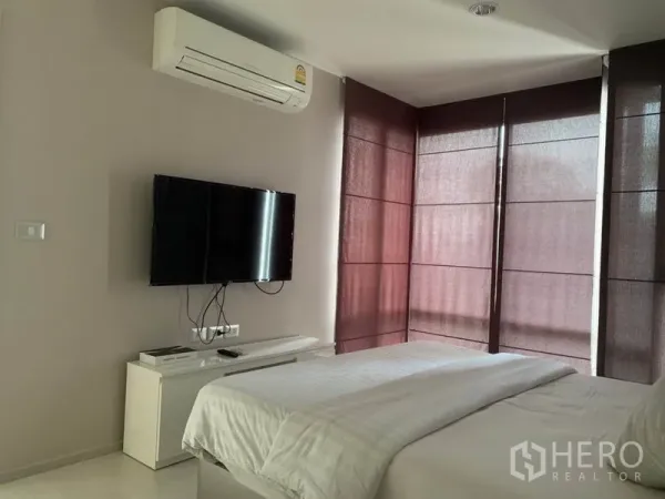 Condominium for rent in Khlong Toei, Bangkok - Bedroom corner featuring wall-mounted TV, air conditioner, and wraparound windows.