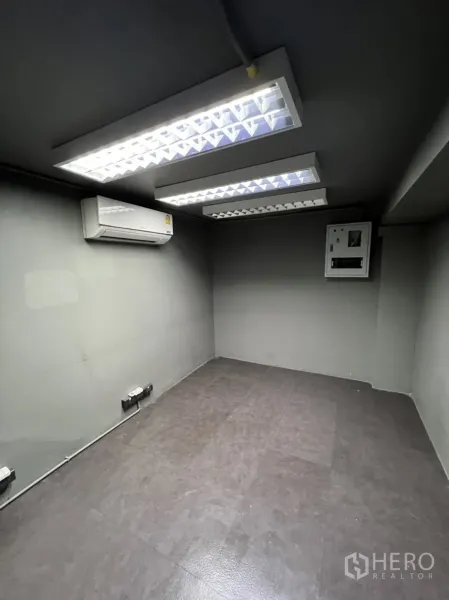 店屋 出租在Phra Khanong, Bangkok - 小型办公室，吊顶日光灯、分体空调与配电箱，灰色墙面