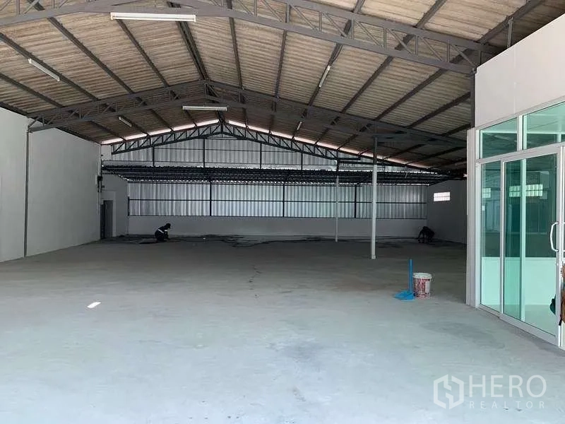 Warehouse for rent in Mueang Pathum Thani, Pathum Thani - Spacious warehouse interior with high steel truss roof, concrete floor and glass entry doors.