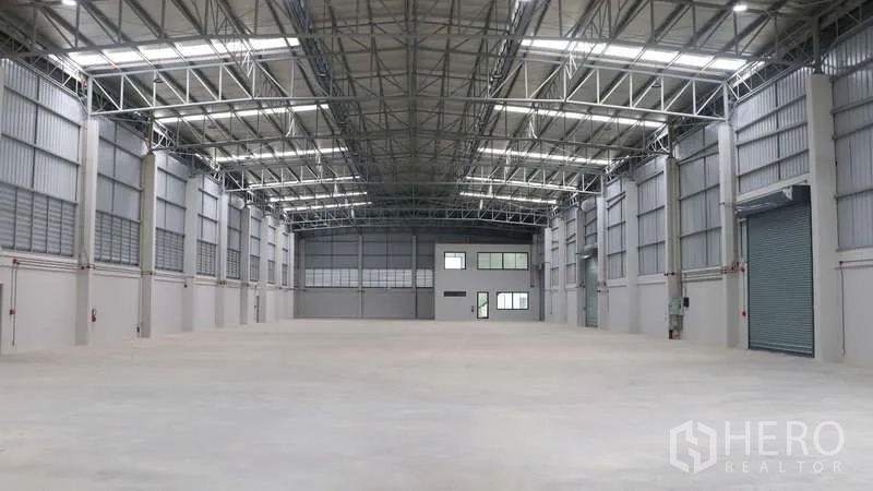 Warehouse for rent in Sam Phran, Nakhon Pathom - Large clear‑span interior with steel roof trusses, bright lighting and shuttered loading door.