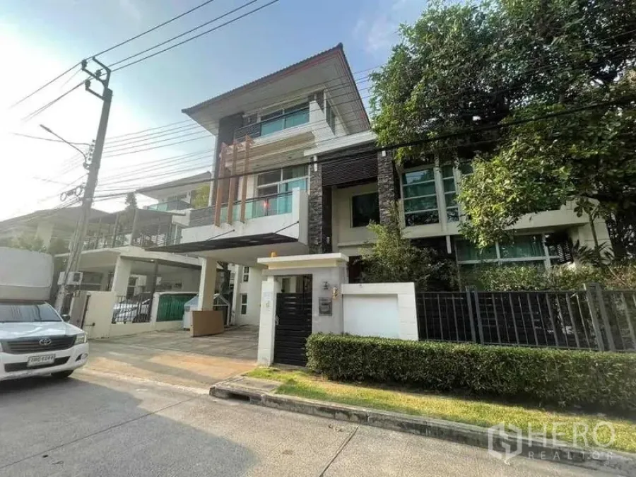Detached House for rent or sale in Khan Na Yao, Bangkok - Street view of the home showing front gate, driveway, carport and greenery in a premium neighborhood.