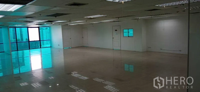 Office Space for rent in Huai Khwang, Bangkok - Vacant office interior showing large tinted windows, multiple doors and reflective floors beneath a suspended ceiling.