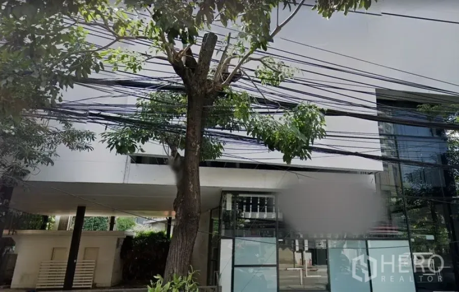 Retail Space for rent in Khlong Toei, Bangkok - Modern low-rise building facade with tall glass windows and roadside trees.