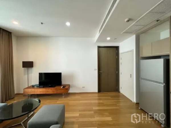 Condominium for rent in Khlong Toei, Bangkok - Bright living room with wooden floors, floating TV console and floor lamp beside the entry to the kitchen in a Phrom Phong condo.